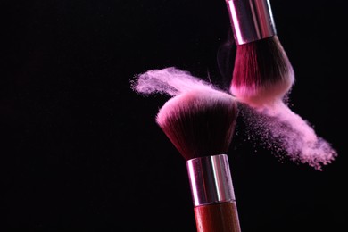 Photo of Makeup brushes with pink eye shadow on black background, closeup. Space for text
