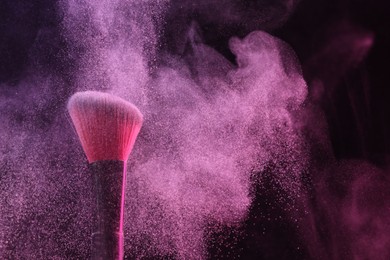 Photo of Makeup brush with pink eye shadow in neon light on black background, closeup. Space for text