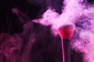 Photo of Makeup brush with pink eye shadow in neon light on black background, closeup. Space for text
