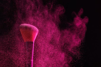Photo of Makeup brush with pink eye shadow on black background, closeup