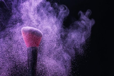 Photo of Makeup brush with purple eye shadow on black background, closeup