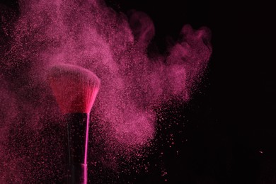 Photo of Makeup brush with pink eye shadow on black background, closeup