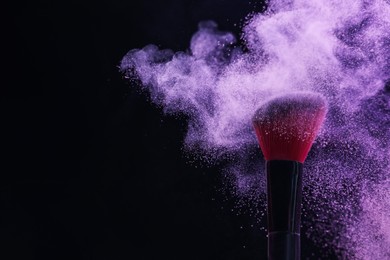 Photo of Makeup brush with purple eye shadow on black background, closeup