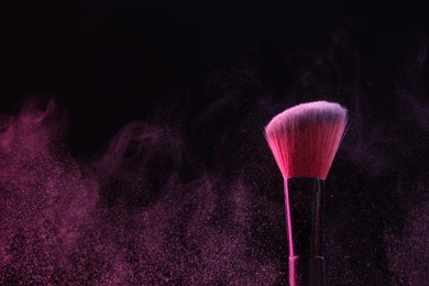 Photo of Makeup brush with pink eye shadow on black background, closeup
