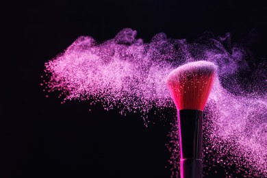 Photo of Makeup brush with pink eye shadow on black background, closeup