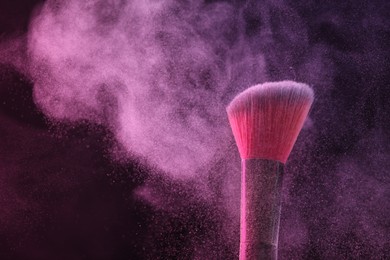 Photo of Makeup brush with pink eye shadow on black background, closeup