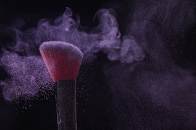 Photo of Makeup brush with purple eye shadow on black background, closeup