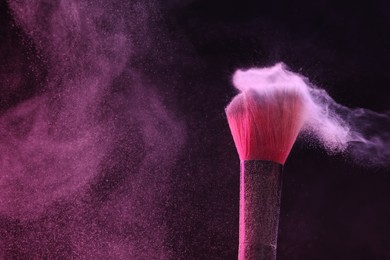 Photo of Makeup brush with pink eye shadow on black background, closeup