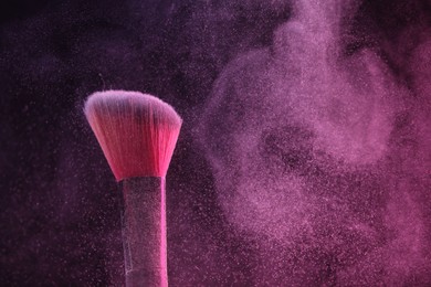 Photo of Makeup brush with pink eye shadow on black background, closeup