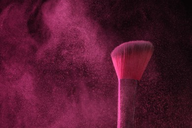 Photo of Makeup brush with pink eye shadow on black background, closeup