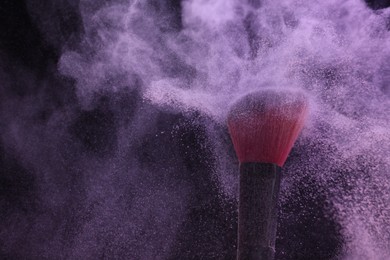 Photo of Makeup brush with purple eye shadow on black background, closeup