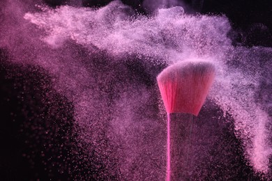Photo of Makeup brush with pink eye shadow on black background, closeup
