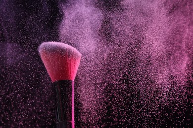 Photo of Makeup brush with pink eye shadow on black background, closeup