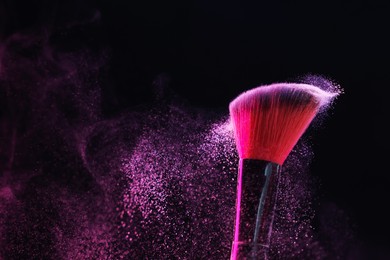 Photo of Makeup brush with pink eye shadow on black background, closeup