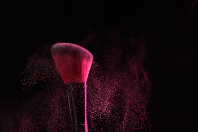 Photo of Makeup brush with pink eye shadow on black background, closeup