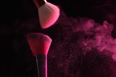 Photo of Makeup brushes with pink eye shadow on black background, closeup. Space for text