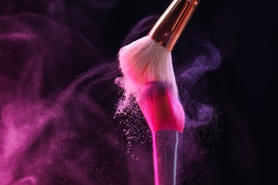 Photo of Makeup brushes with colorful eye shadows in neon lights on black background, closeup