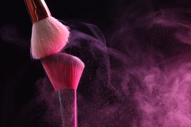 Photo of Makeup brushes with pink eye shadow on black background, closeup. Space for text