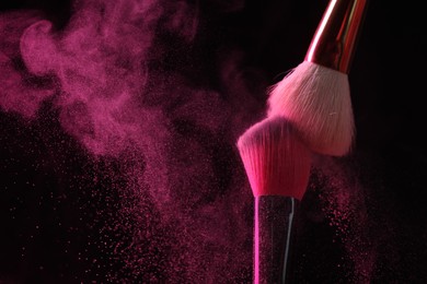 Photo of Makeup brushes with pink eye shadow on black background, closeup. Space for text