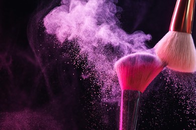 Photo of Makeup brushes with color eye shadow in neon lights on black background, closeup. Space for text