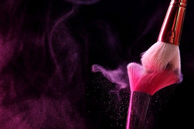 Photo of Makeup brushes with color eye shadow in neon lights on black background, closeup. Space for text