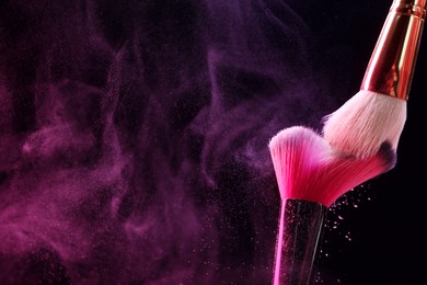 Photo of Makeup brushes with color eye shadow in neon lights on black background, closeup. Space for text
