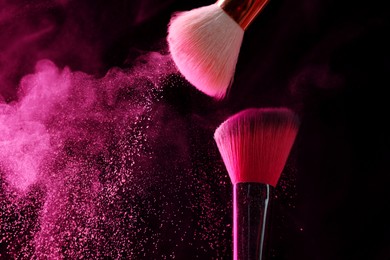 Photo of Makeup brushes with pink eye shadow in neon lights on black background, closeup. Space for text