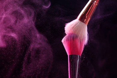 Photo of Makeup brushes with pink eye shadow in neon lights on black background, closeup. Space for text