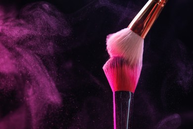 Photo of Makeup brushes with pink eye shadow in neon lights on black background, closeup. Space for text
