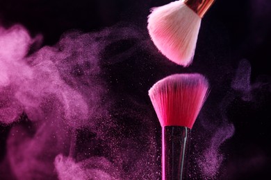 Photo of Makeup brushes with pink eye shadow in neon lights on black background, closeup. Space for text