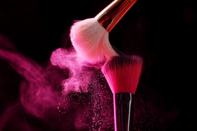 Photo of Makeup brushes with pink eye shadow on black background, closeup