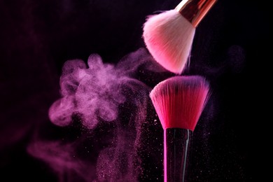 Photo of Makeup brushes with pink eye shadow on black background, closeup. Space for text