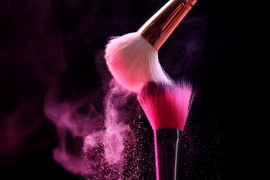 Photo of Makeup brushes with pink eye shadow on black background, closeup. Space for text