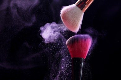 Photo of Makeup brushes with purple eye shadow on black background, closeup. Space for text