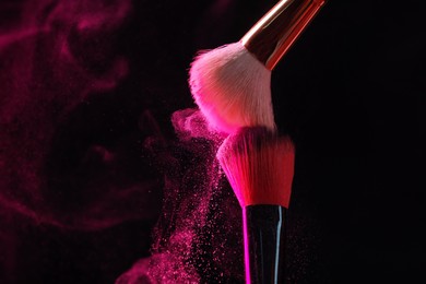 Photo of Makeup brushes with pink eye shadow on black background, closeup. Space for text