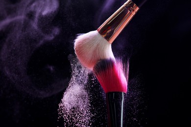 Photo of Makeup brushes with purple eye shadow on black background, closeup