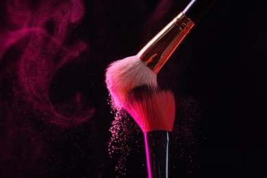 Photo of Makeup brushes with pink eye shadow on black background, closeup