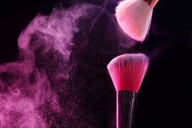 Photo of Makeup brushes with pink eye shadow on black background, closeup. Space for text