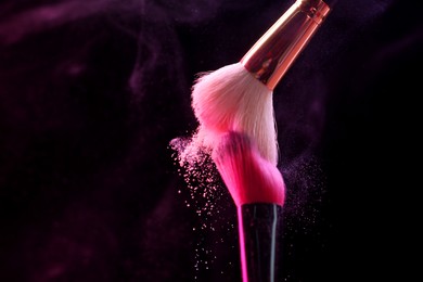 Photo of Makeup brushes with colorful eye shadows in neon lights on black background, closeup. Space for text