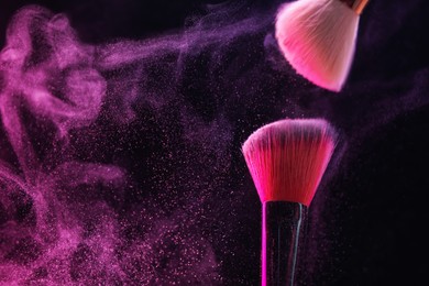 Photo of Makeup brushes with pink eye shadow on black background, closeup. Space for text