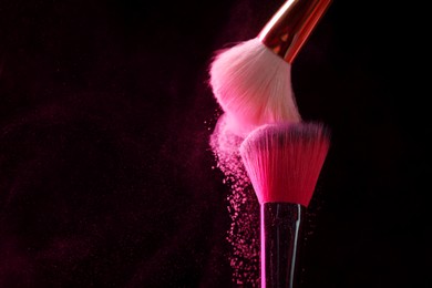 Photo of Makeup brushes with pink eye shadow on black background, closeup. Space for text
