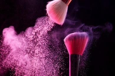 Photo of Makeup brushes with pink eye shadow on black background, closeup. Space for text