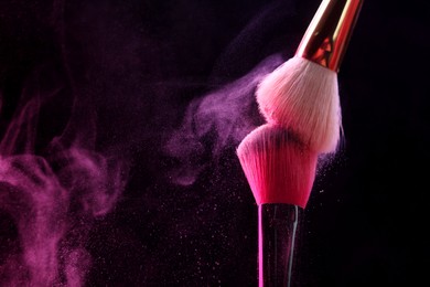 Photo of Makeup brushes with pink eye shadow on black background, closeup. Space for text