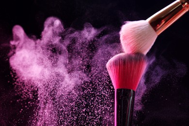 Photo of Makeup brushes with pink eye shadow on black background, closeup. Space for text