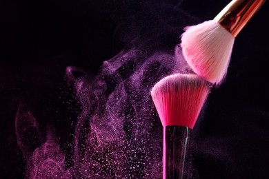 Photo of Makeup brushes with pink eye shadow on black background, closeup. Space for text