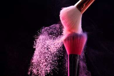 Photo of Makeup brushes with pink eye shadow on black background, closeup. Space for text