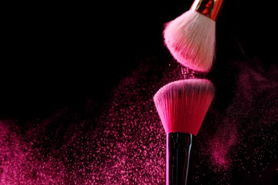 Photo of Makeup brushes with pink eye shadow on black background, closeup. Space for text