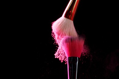 Photo of Makeup brushes with pink eye shadow on black background, closeup. Space for text