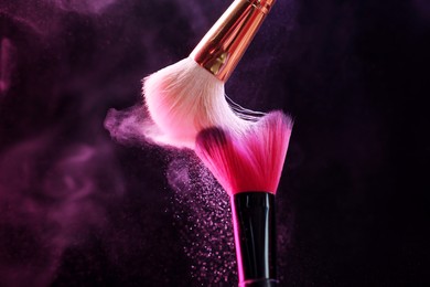 Photo of Makeup brushes with colorful eye shadows in neon lights on black background, closeup