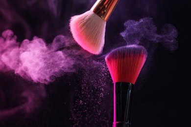 Photo of Makeup brushes with colorful eye shadows in neon lights on black background, closeup
